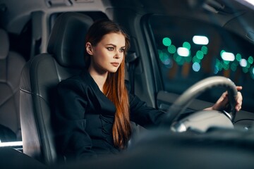 horizontal photo of a nice woman in a black shirt driving a car while driving at night