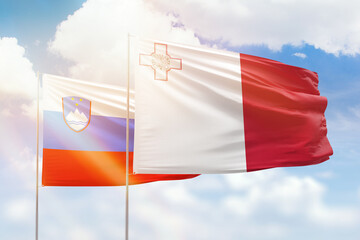Sunny blue sky and flags of malta and slovenia