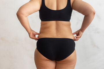 Cropped rearview of fat, adipose, overweight female body in black underwear, checking and holding excess folds, sides on back. Cellulite friable skin problem. Dieting and unhealthy eating problem - obrazy, fototapety, plakaty