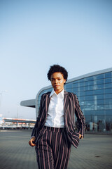4k. Travel, Digital. Charming African American woman in modern striped suit stands by the glass...