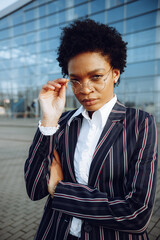 4k. Charming African American woman in modern striped suit stands on background of glass wall in...