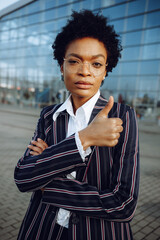 4k. Charming African American woman in modern striped suit stands on background of glass wall in...