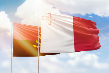 Sunny blue sky and flags of malta and angola