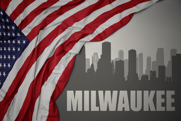 abstract silhouette of the city with text Milwaukee near waving national flag of united states of america on a gray background.