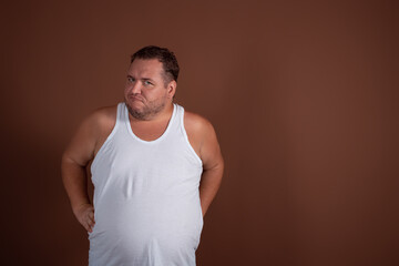 An angry fat guy in a white T-shirt screams in disgust against a brown background.