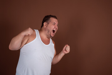 An angry fat guy in a white T-shirt screams in disgust against a brown background.