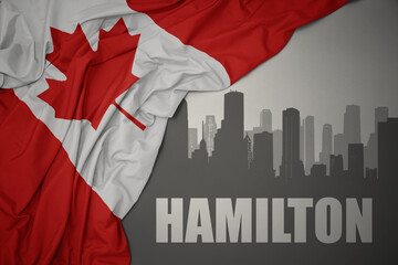 abstract silhouette of the city with text Hamilton near waving national flag of canada on a gray background.