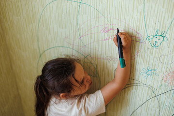 Top view of little naughty girl with dark hair wearing T-shirt, holding green marker in hand,...