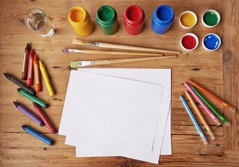 Creativity never goes out of style. Blank white paper with painting supplies and pencils on a...