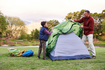 Camp is almost ready. Shot of a father and son setting up a tent together while camping.