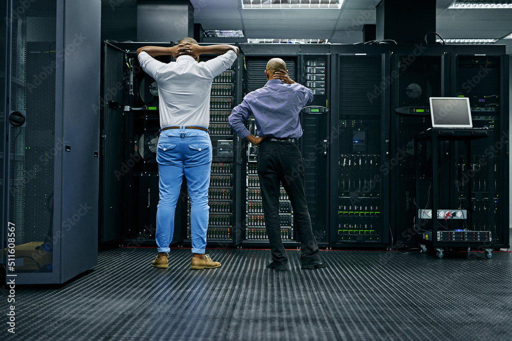 Poster meanwhile in the server room.... rearview shot of two it technicians having difficulty repairing a c