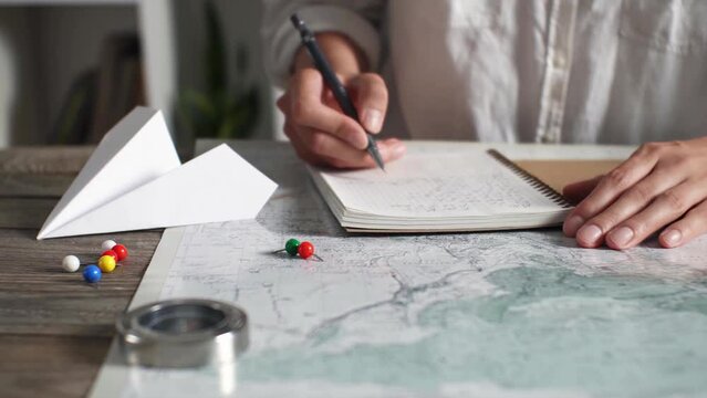 A tourist takes notes in a diary on the background of a map of a laid route, planning a trip in anticipation of a vacation summer vacation with adventure, writes down location coordinates
