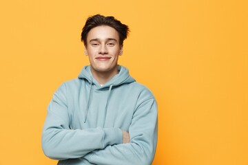 a close horizontal photo of a handsome young man standing on an orange background in a light blue hoodie with his arms crossed over his chest