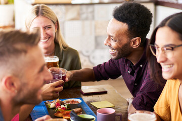 Group of funny multicultural people drink beer in a bar. 30s Young friends having fun and having lunch and alcohol in a rooftop happy hour.