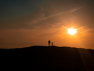 The boy leads his father through the hills towards the sun. Beautiful sunset Silhouette