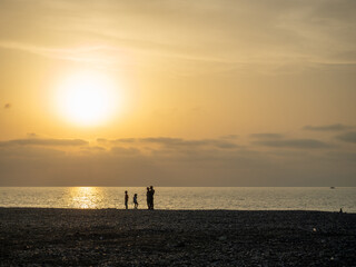 Silhouettes of people against the backdrop of a bright sunset. Orange sunset. Family on vacation. ...