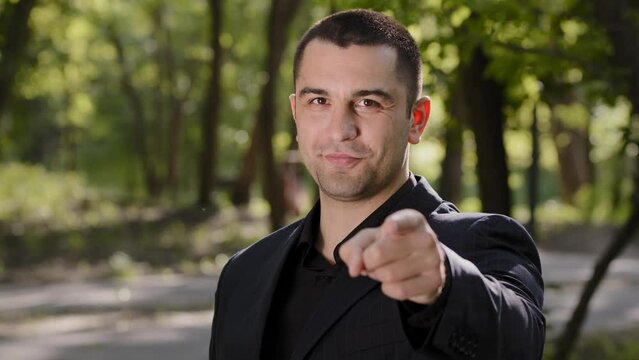 Cheerful confident adult businessman guy show hey you gesture points finger at camera make best choice handsome caucasian man wears formal suit stand outdoors nods head choose option approve good idea