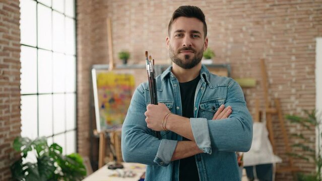 Young hispanic man smiling confident standing with arms crossed gesture at art studio