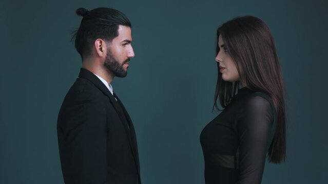 Seductive man and sexy woman looking each other in the eye, standing face to face, experiencing intense emotions. Dark green background studio shot. High quality 4k footage