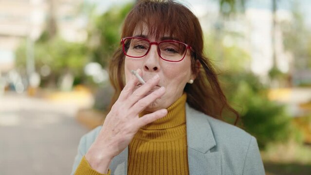 Middle age woman business executive smoking cigarette at park