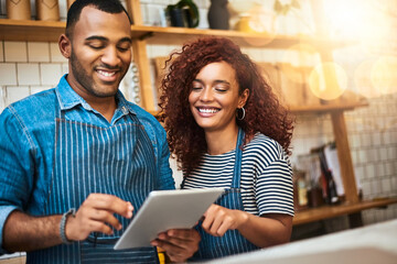 Coming up with great ideas together. Cropped shot of an affectionate young couple working on a tablet in their coffee shop.