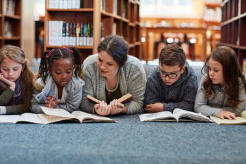 Reading is fundamental. Cropped shot of elementary school kids reading with their teacher on the...