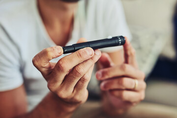 I still need to work out how to use this properly. Shot of a unrecognizable man holding a insulin test blood sample with his hands while being seated on a couch at home.