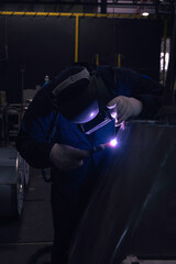 Naklejka na ściany i meble Skillful welders weld stainless steel in the factory. Construction site metal welder. builder wear fireproof gloves for safety at work.