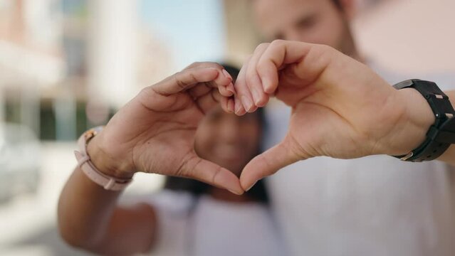 Man and woman interracial couple doing heart gesture with hands at street