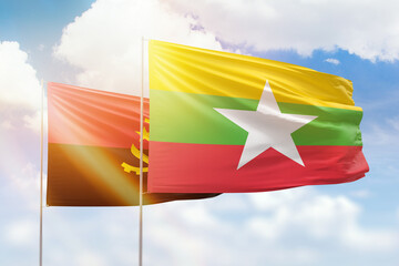 Sunny blue sky and flags of myanmar and angola