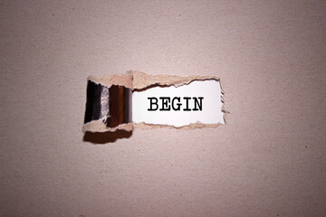The text Begin appearing behind torn brown paper.