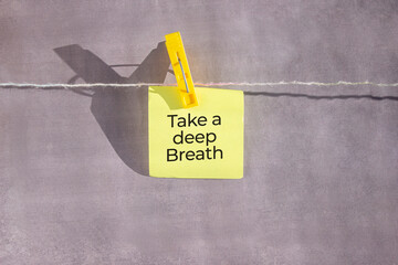 Take a deep breath text on a yellow sticker on a rope with clothespins on a grey background.