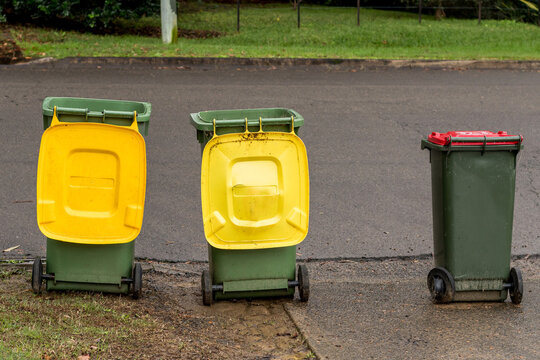 Australian garbage wheelie bins with colourful lids for recycling and general household waste lined up on the street for council rubbish collection