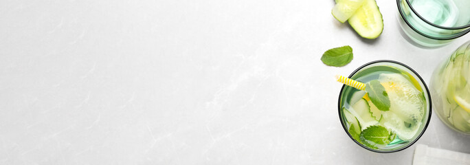 Refreshing water with cucumber, lemon and mint on white table, flat lay with space for text. Banner...
