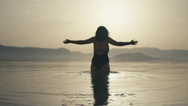 Slow motion video of a girl diving into the sea at sunset in a beautiful landscape. A woman in a bathing suit goes swimming in the ocean.