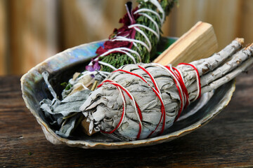 A close up image of two healing smudge sticks with a palo santo smudge stick in an abalone shell. 