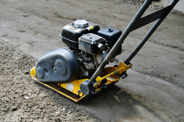 A close up image of a vibrating soil compactor used to compact soil in preparation for paving stones.  - obrazy, fototapety, plakaty