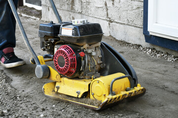 A close up image of a vibrating soil compactor being used to prepare soil for patio stones.