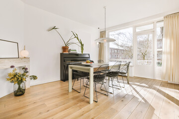 Bright living room with a balcony door, a large window, a piano against the wall and a table with...