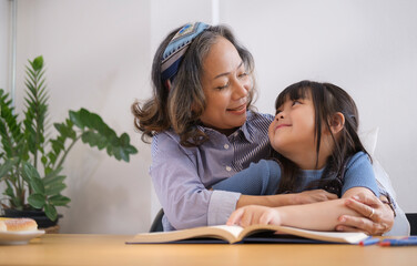 Loving grandmother reading a book to her little granddaughter, enjoying free time on weekend at home together.
