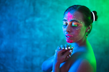 Young woman with closed eyes in fluorescent body art on posing in ultraviolet light. Bright abstract drawings in colorful neon lighting, copy space.