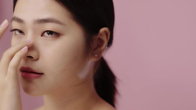 Close up face of beautiful young Asian woman with clear skin on pink background.