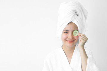 Young beautiful asian girl caucasian smiling hiding eye behind cucumber slice over white background. Beauty spa skin care therapy and cosmetology concept.