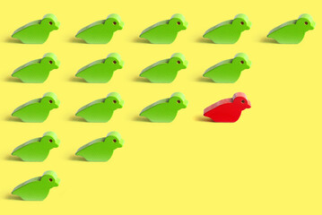 The different concept with a red wooden toy bird among many green ones on a yellow background.