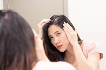 Asian Beautiful woman are looking herself in mirror and use hand touch her hair and looking for  grey hair or hair loss with worry face.