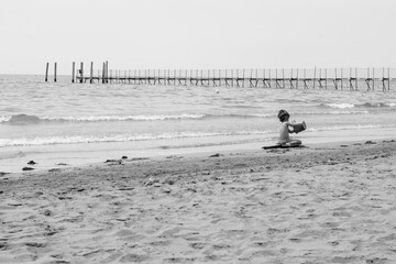 the child happily plays on the sand in front of the sea and an old pier