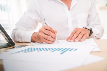 A man holding a pen with business reports, making a work plan and writting on paper on wooden office desk with laptop.