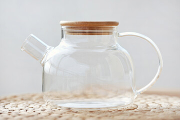 Closeup empty glass teapot with wooden lid on wicker tablemat. Eco-friendly tableware