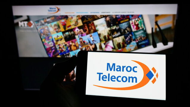 Stuttgart, Germany - 02-13-2022: Person holding mobile phone with logo of telecommunications company Maroc Telecom (IAM) on screen in front of web page. Focus on phone display.