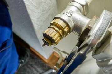 Hand replace old radiator thermostat valve. Pliers removes component from the heater. Modernization...